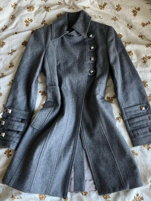 Grå kappa med silvriga detaljer - Den kan stängas med knapparna och dubbel dragkedja. Text med glittrande stenar / rhinestones finns inuti. Dragkedjan kräver att man sliter i den extra eftersom den är lite svår att dra upp i början, men det går säkert att lösa med någon form av vax eller olja. Det finns två riktiga fickor. Axelbredd: 42 cm 🌸Längd: 85 cm 🌸Armlängd: 61 cm 🌸Midjebredd: 40 cm