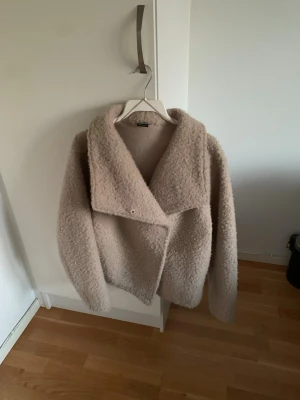 Mysig vårjacka Gina Tricot - Ej använd. Passar S och M. Mysig beige teddyjacka med bred krage och asymmetrisk knäppning. Jackan har en fluffig och mjuk struktur som ger en trendig look. Perfekt för kyliga dagar när du vill vara både varm och snygg.
