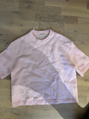 Ljusrosa stickad tröja Gina Tricot - Supersöt ljusrosa stickad tröja från Gina Tricot i kortare modell med rund halsringning och ribbade kanter. Tröjan har korta ärmar och är gjord i ett mjukt, mysigt material som känns skönt mot huden. Perfekt för dig som gillar en enkel men trendig look.