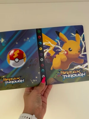 Pokémon Break Through samlarpärm - Säljer en Pokémon Break Through samlarpärm med Pikachu på framsidan och färgglada motiv. Pärmen har plastfickor för att förvara och organisera samlarkort. Perfekt för dig som vill hålla ordning på dina Pokémonkort och visa upp din samling. Plats för 240 st kort 