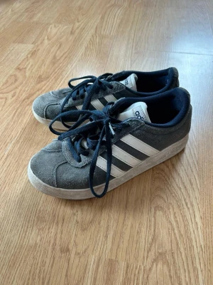 Adidas grå sneakers med vita ränder - Klassiska Adidas sneakers i grå mocka och vit sula. Skorna har mörkblåa snören och innerfoder. Fina ju. 36 och2/3. Skriv om ni vill ha fler bilder eller vid funderingar! mvh!