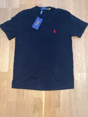 Svart t-shirt från Polo Ralph Lauren - Klassisk svart t-shirt från Polo Ralph Lauren med röd broderad logga på bröstet. T-shirten har rund halsringning och korta ärmar. Tillverkad i mjuk bomull för en skön känsla och enkel stil.