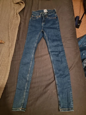 Blå skinny jeans  - Säljer ett par klassiska blå skinny jeans från Lager 157 i storlek XS. Jeansen har fem fickor, dragkedja och knapp framtill samt smala ben. Perfekta för dig som gillar en tajt passform och enkel stil. Modellen snake