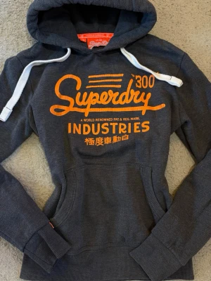 Superdry marinblå hoodie vintage S - Vintage hoodie från Superdry med stort orange tryck på bröstet och vita dragsnören i huvan. Lite sprucken logga, annars bra skick💕💕