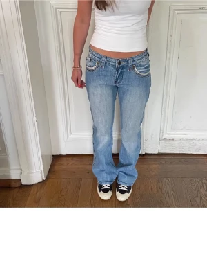 Ljusblå bootcut jeans med detaljer - Säljer ett par ljusblå bootcut jeans med slitningar och snygga sömdetaljer vid fickorna. Köpt för 500 men alldrig andvänt! Storlek S, köpt på Plick. Bilden är från den jag köpte ifrån! 