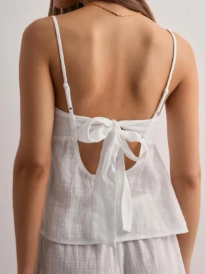 Vit linnetopp med knyt i ryggen - Superfin vit linnetopp med tunna axelband och snygg knytning i ryggen. Toppen är ärmlös och har en luftig, lätt struktur som passar perfekt till varma dagar. Materialet känns svalt och fräscht, och toppen har en avslappnad passform.