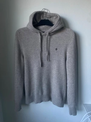 Beige stickad hoodie från Morris - Snygg beige stickad hoodie från Morris med broderad logga på bröstet. Tröjan har en defekt se sista bilden men går lätt att fixa med nål och tråd😊