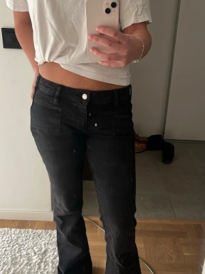 Svarta bootcut jeans med fickor - Säljer ett par svarta bootcut jeans med fram- och bakfickor. Jeansen har låg midja och klassisk knappstängning. Snygg passform som sitter tajt upptill och släpper vid benen. Perfekta för dig som gillar en stilren och trendig look.