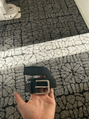 Jack and Jones bälte - Snyggt svart flätat bälte med ett stilrent silverfärgat metallspänne. Bältet har detaljer i skinn vid ändarna och passar perfekt till jeans eller chinos. Enkel att justera tack vare det flexibla materialet och den klassiska designen.