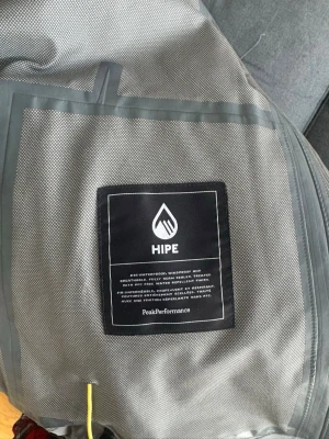 Grå vindjacka Peak Performance HIPE - Snygg grå vindjacka från Peak Performance med HIPE-material som är vattentätt, vindtätt och andas. Jackan har tejpade sömmar och sportig design, perfekt för utomhusaktiviteter och äventyr. Jackan passade inte så därav till salu.