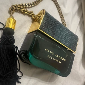 Marc Jacobs Decadence parfym - Säljer en lyxig Marc Jacobs Decadence parfym. Flaskan är formad som en handväska med en elegant kedja och en svart tofs. Perfekt för den som vill ha en doft med stil och elegans. Jag har fortfarande två kvar av den parfymen för jag älskade den förut men nu blev jag lite trött på den så tänkte sälja en av dom🤍. Den är 100ml och ändast testad en gång