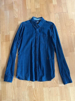 Blå prickig skjorta Scotch & Soda - Snygg blå skjorta från Scotch & Soda med små vita prickar och klassisk krage. Skjortan har lång ärm, knappar framtill och en bröstficka. Tillverkad i mjuk bomull som känns skön mot huden. Perfekt för dig som gillar stilrena detaljer.