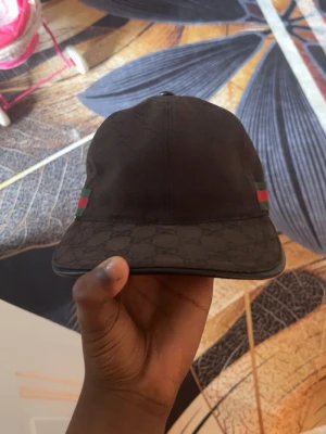 Svart Gucci keps med logga är äkta  - Snygg svart keps från Gucci med klassiska gröna och röda ränder på sidorna. Skärmen har diskret GG-mönster och kepsen är tillverkad i Italien. Justerbar rem baktill för perfekt passform. Perfekt accessoar för en trendig streetwear-look.den är äkta .