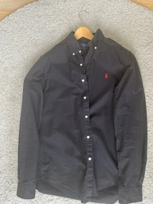 Svart skjorta från Ralph Lauren - Svart skjorta från Ralph Lauren, custom fit. Skjortan är i storlek m och är i mycket bra skick. Tecken på användning är få och små. Pris kan diskuteras, skriv gärna vid intresse 