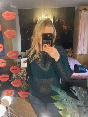 Mörkgrön prickig meshblus - Snygg mörkgrön meshblus med prickigt mönster och transparent material. Blusen har långa ärmar med lätt puff och resår vid ärmslut. Perfekt att styla med ett linne under för en trendig look.