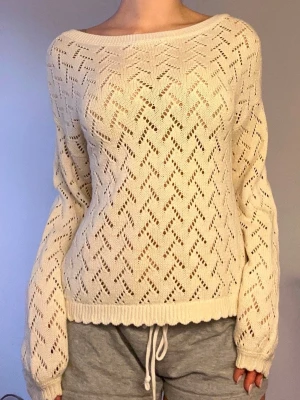 Benvit stickad tröja med hålmönster - Säljer en vit stickad tröja med snyggt hålmönster och rundad halsringning. Tröjan har långa ärmar och ribbad kant nedtill. Perfekt för lager på lager och ger en chill vibe till din outfit.