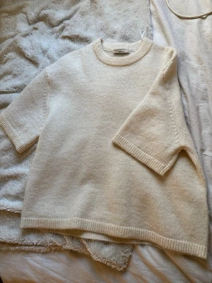 Krämvit stickad tröja Gina Tricot - Krämvit stickad tröja från Gina Tricot med rund halsringning och halvlånga ärmar. Tröjan har ribbade muddar vid hals, ärmslut och nederkant. Tillverkad i mjukt material som ger en avslappnad och trendig look.