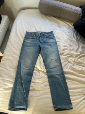 Ljusblå raka jeans Jack & Jones - Säljer ett par ljusblå jeans från Jack & Jones med klassisk rak passform. Jeansen har fem fickor, bälteshällor och knappgylf. Tillverkade i slitstark denim med snygg tvättad look. Perfekta för en avslappnad stil.