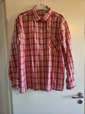 Rödvit rutig skjorta i bomull, stl 48, Wästgöta - Klassisk röd och vit rutig skjorta från Wästgöta. Skjortan har lång ärm, bröstficka och knappar framtill. Perfekt för en avslappnad och stilren look.