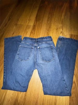 Blå Bootcut  jeans med hög midja - Säljer ett par klassiska blå jeans med raka ben och hög midja. Jeansen har fem fickor, bälteshällor och stängs med knapp och dragkedja. Perfekta till vardagslooken och passar till det mesta. Materialet är denim i bomull.