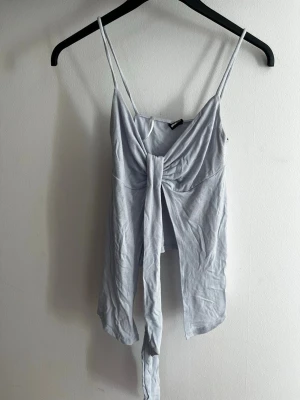 Ljusblå linnetopp från Gina Tricot - Trendig ljusblå linnetopp från Gina Tricot med smala axelband och snygg knytning framtill. Toppen är ärmlös och har en croppad passform som passar perfekt till höga jeans eller kjol. Tillverkad i mjukt material för en bekväm känsla. Aldrig använd