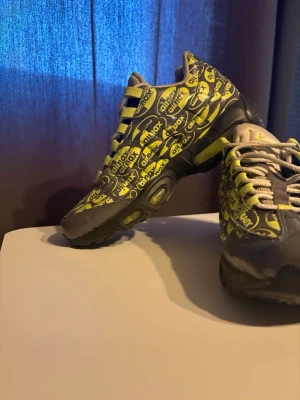 Buty Nike Air Max 95  - Nike Air Max 95 sneakers med svart och Neon färg, täckt av upprepade 'airmax'-loggor. Skorna har en chunky sula med synliga luftbubblor och snörning framtill. Materialet är en mix av textil och syntet. Perfekt för dig som gillar statement-sneakers.