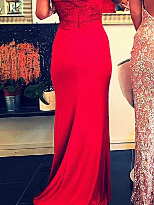 Balklänning.Röd offshoulder långklänning spets - Snygg röd långklänning med offshoulder-modell och figurnära passform. Överdelen har fina spetsdetaljer och broderier som ger en elegant känsla. Kjolen är slät och faller mjukt ner till golvet. Perfekt för bal eller student.