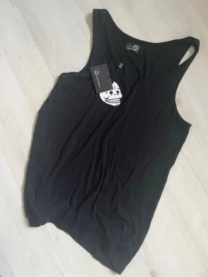 Svart linne från Dedicated Cheap Monday - Snyggt svart linne från cheap Monday Dedicated med rund halsringning och avslappnad passform. Perfekt till jeans eller shorts för en enkel och clean look. Tillverkat i mjuk bomull som känns skön mot huden. Litet tryck med logga i nacken.