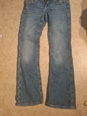 Blå bootcut jeans med broderade fickor - Säljer ett par klassiska blå bootcut jeans med snygga broderade detaljer på bakfickorna. Perfekta för dig som gillar en avslappnad men ändå trendig stil.