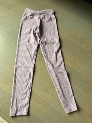 Ljuslila ribbade leggings - Säljer ett par ljuslila leggings med smala ribbade ränder. De har hög midja och är i ett mjukt, stretchigt material som sitter skönt på kroppen. Perfekta för en chill och avslappnad stil.