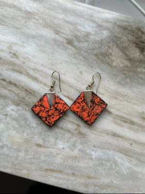 Orange geometriska örhängen 80-tal - Unika örhängen i diamantform med stark orange färg och svarta marmorerade detaljer. Örhängena har en metallisk trekant upptill och krokfäste. Perfekt för dig som vill sticka ut med ett coolt och färgstarkt smycke.