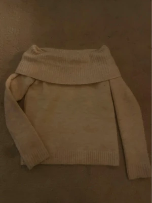 Beige off shoulder stickad tröja - Säljer en beige stickad tröja med bred off shoulder-krage och långa ärmar. Tröjan har ribbstickade muddar vid ärmslut och nederkant, vilket ger en snygg och avslappnad look. Perfekt för dig som gillar en enkel men trendig stil. Storlek -146/152 men passar också xxs 