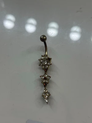 Guldigt örhänge med stjärnformade pärlor - Unikt örhänge i guldton med tre stjärnformade hängen, dekorerade med små vita pärlor och gnistrande stenar. Böjd stav med kula upptill ger en cool look. Perfekt för dig som vill sticka ut med detaljerade accessoarer.