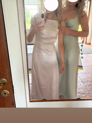 Ljusrosa balklänning i satin - Elegant ljusrosa långklänning i satin med draperad v-ringning och smala axelband. Klänningen har en mjuk glans och följsam passform som framhäver siluetten. Perfekt för student eller bal. Snygg och stilren design som känns lyxig. Skriv vid frågor! Varan är använd 1 gång! Orginal pris 1000kr