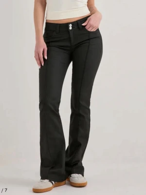Skinnbyxor från Nelly  - Snygga svarta bootcut skinnjeans med markerade pressveck framtill och dubbla knappar i midjan. Jeansen har klassisk femficksmodell och bälteshällor. Materialet ser ut att vara stretchigt denim för en bekväm passform.
