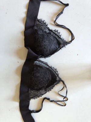 Svart spetsbralette med tunna band - Snygg svart bralette med triangelformade kupor i blommig spets och tunna justerbara axelband. Bh:n har dekorativa spetskanter och bredare band under bysten för extra komfort. Perfekt för dig som gillar en feminin och stilren look.