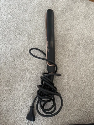 Svart och kopparfärgad plattång - Säljer en stilren plattång i svart med kopparfärgade plattor och detaljer. Den har sladd med vanlig stickkontakt och smal, avlång form som gör den enkel att använda för styling av håret. Perfekt för att fixa frisyren snabbt och smidigt.