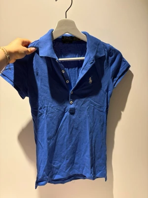 Blå pikétröja från Polo Ralph Lauren - En blå piké från Ralph Lauren, den är använd typ en gång men jag passar inte i blått så tyvärr måste den säljas. Den är så fin! 