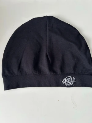 Syna skull cap - Svart mössa från SVEA med en stilren, broderad logga i vitt framtill. Tillverkad i mjuk bomull som sitter skönt på huvudet. Enkel och clean design som passar till det mesta och ger en avslappnad vibe.