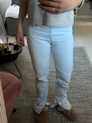 Ljusblå raka jeans - Säljer ett par ljusa ljusblå (nästan vita)  jeans med rak passform och klassisk femficksdesign. Jeansen har hög midja och perfekta till våren/sommaren. Slits nertill. Slitna i nederkant.