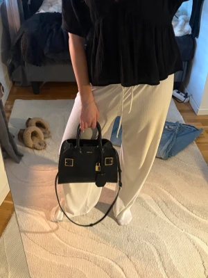 Svart handväska från ALDO - Snygg svart handväska från ALDO med guldfärgade detaljer och spännen. Väskan har både handtag och en avtagbar axelrem, samt dekorativt hänglås framtill. Stilren och strukturerad modell i konstläder med croco-mönster.