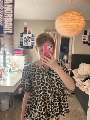 Leopardmönstrad blus med puffärm - Snygg blus med leopardmönster och puffiga korta ärmar. Modellen har tre knytband framtill och en luftig, volangig passform. Perfekt för dig som vill sticka ut med ett djurmönster. Materialet känns lätt och skönt mot huden.