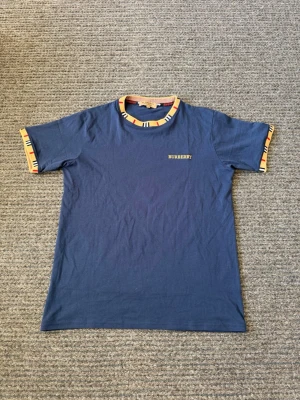 Burrberry t-shirt - Snygg blå t-shirt från Burberry med klassisk logga broderad på bröstet. T-shirten har korta ärmar och unika mönstrade kanter i beige, svart och rött runt halsringning och ärmslut. Tillverkad i mjuk bomull för skön känsla.