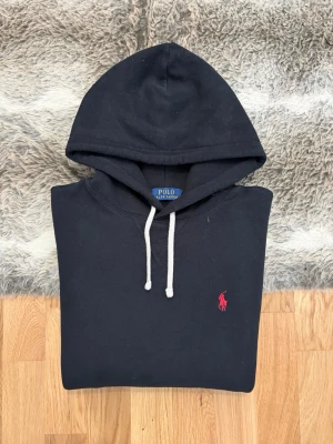 Svart Hoodie Från Polo Ralph Lauren - Hej! 👋 Säljer en riktigt fräsch svart Polo Ralph Lauren hoodie i storlek S. Den har den eftertraktade röda pony-loggan på bröstet – en tidlös favorit! 🐎 Tröjan är i mycket gott skick, djupsvart och supermjuk på insidan ✨ Denna modell har även QR-kod för enkel verifiering av äkthet direkt i mobilen ✅ Sitter perfekt på (Modell: 177cm) 👕 Ett premium-basplagg som passar till precis allt. Först till kvarn! Fraktar snabbt 🚛📦💬💯 