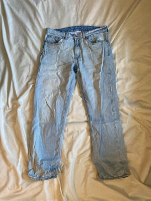 Ljusblå raka jeans från Levi's - Säljer ett par klassiska ljusblå jeans från Levi's med rak passform och fem fickor. Jeansen har normal midja och är tillverkade i slitstark denim. Perfekta för en avslappnad och trendig look.