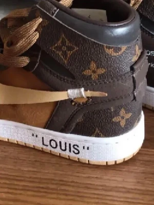 Bruna High sneakers - Unika sneakers med brunt och beige monogrammönster. Skorna har högt skaft, perforerad tå och bruna skosnören. Materialet är en mix av läder och canvas med klassiska loggor och vit sula.