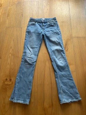 Ljusblå bootcut jeans med rå kant - Säljer ett par ljusblå bootcut jeans med rå, fransad kant nedtill. Jeansen har klassisk femficksmodell och normal midja. Perfekta för dig som gillar en avslappnad och trendig look. Materialet är denim i bomull.