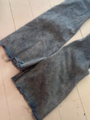 Blå raka jeans med råa kanter - Säljer ett par ljusblå raka jeans med slitna, råa kanter nertill. Jeansen har klassisk femficksdesign och en tvättad look som ger en avslappnad vibe. Materialet är denim i bomull. Perfekta för dig som gillar en trendig och avslappnad stil.