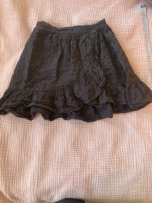 Svart volangkjol med struktur - Säljer en svart kortkjol med volangkant och snyggt strukturerat tyg. Kjolen har en elastisk midja som gör den bekväm och lätt att bära. Perfekt för dig som gillar en cool och avslappnad stil med lite extra detaljer.