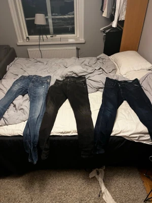 Tre par jeans i olika tvättar - Säljer tre par jeans i olika färger: ett par ljusblå, ett par svarta och ett par mörkblå. Alla har klassisk femficksdesign och smal passform. Perfekta för dig som gillar att variera din stil med olika tvättar och färger.